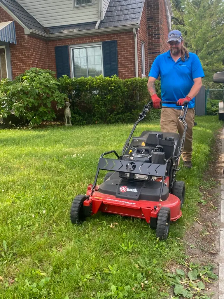 Professional landscaper mowing a residential lawn with a push lawn mower, showcasing quality lawn care services.