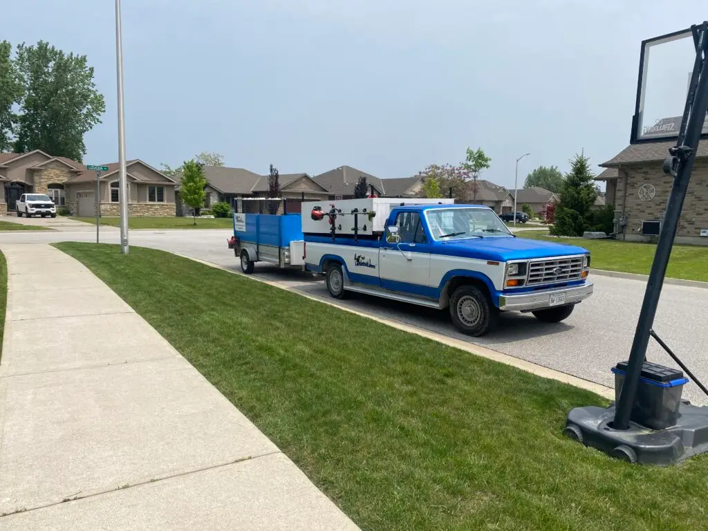 Blue and white landscaping truck parked on a residential street, equipped with tools for lawn care and maintenance, showcasing a commitment to quality landscaping services in the neighborhood.