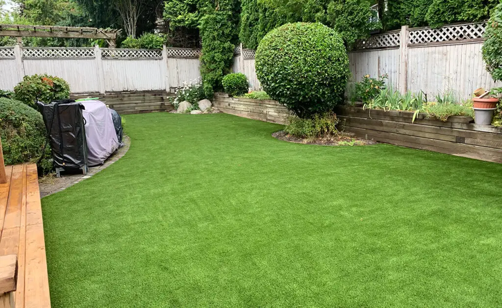 Lush green artificial turf in a landscaped backyard featuring well-maintained shrubs, wooden planter boxes, and a cozy seating area, showcasing a low-maintenance outdoor space ideal for relaxation and entertainment.